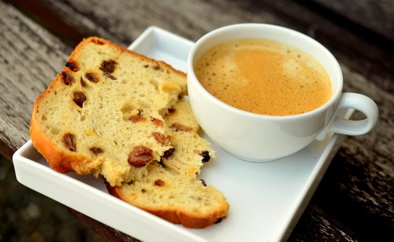 Fresh espresso beside thick slices of fruit bread.