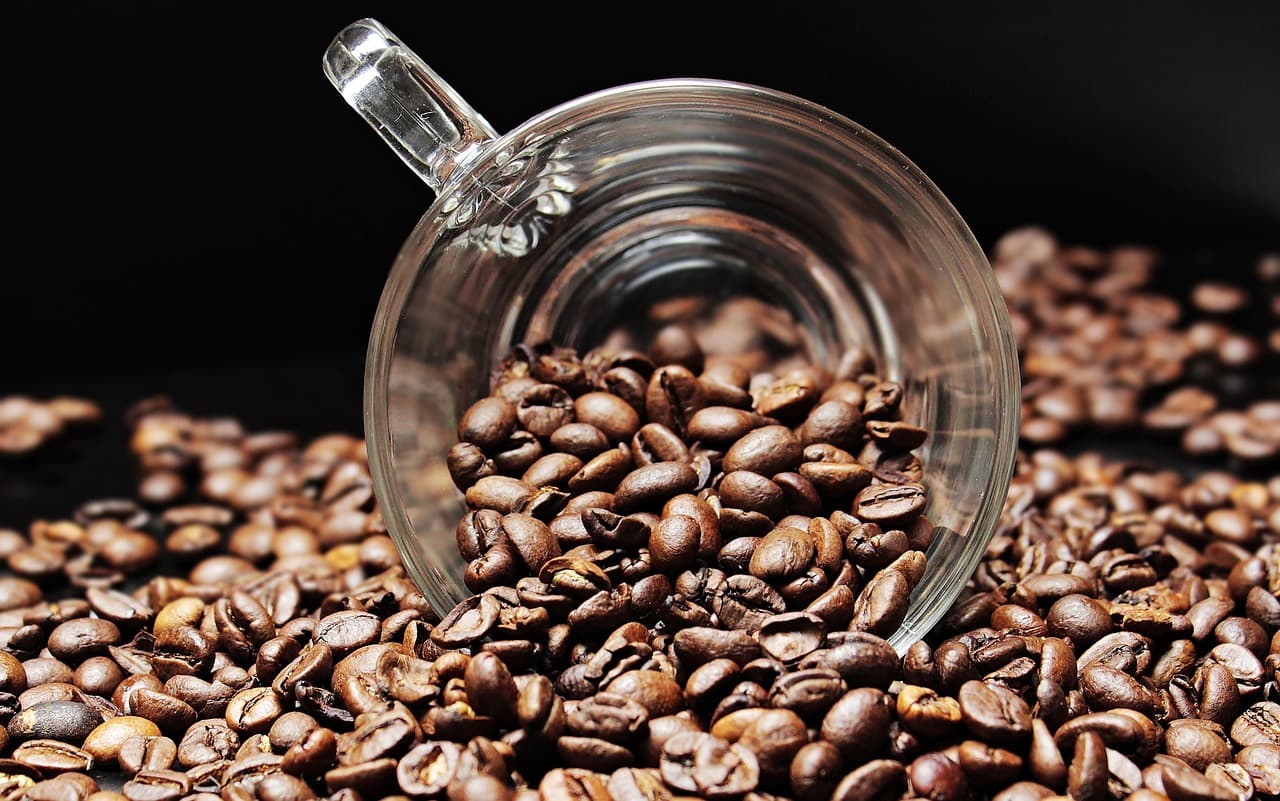 Roasted coffee beans spilling from a glass mug.