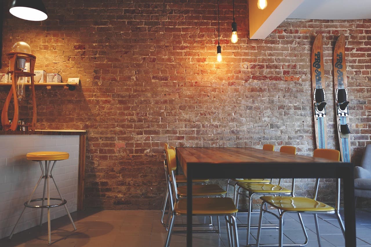 Warm brick cafe interior with a communal table, pendant lights, and a pour-over station.